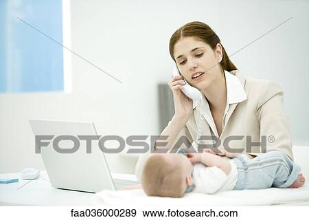 Professional woman touching infant lying on desk, making phone call View Large Photo Image Stock Photo - Professional woman touching infant lying on desk, making phone call. Fotosearch