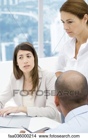 Professionals having a meeting at desk, focus on standing woman View Large Photo Image Picture - Professionals having a meeting at desk, focus on standing woman. Fotosearch