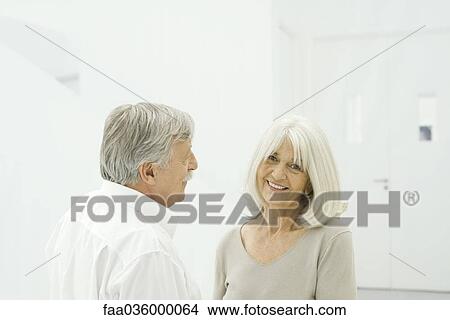 Picture - Senior couple standing face to face, woman smiling at camera. Fotosearch