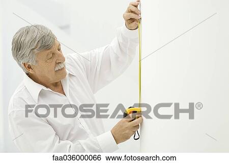 Senior man using measuring tape on wall View Large Photo Image Stock Photograph - Senior man using measuring tape on wall. Fotosearch