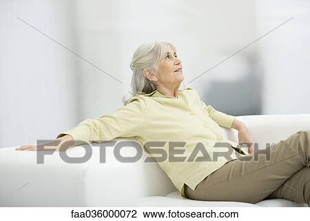 Senior woman sitting on couch, looking up, smiling View Large Photo Image Stock Image - Senior woman sitting on couch, looking up, smiling. Fotosearch