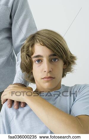 Teen boy holding father's hand on shoulder, looking at camera, cropped view View Large Photo Image Stock Photography - Teen boy holding father's hand on shoulder, looking at camera, cropped view. Fotosearch
