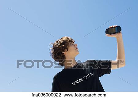 Teen boy holding up handheld video game, wearing tee-shirt printed with the words "game over" View Large Photo Image Stock Image - Teen boy holding up handheld video game, wearing tee-shirt printed with the words "game over". Fotosearch