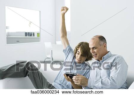 Teen boy showing handheld video game to father, arm raised View Large Photo Image Picture - Teen boy showing handheld video game to father, arm raised. Fotosearch