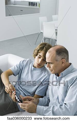 Teen boy showing handheld video game to father View Large Photo Image Stock Image - Teen boy showing handheld video game to father. Fotosearch