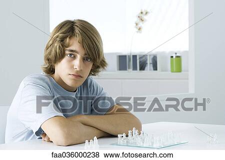 Teen boy sitting at table, playing chess, looking at camera View Large Photo Image Stock Photo - Teen boy sitting at table, playing chess, looking at camera. Fotosearch