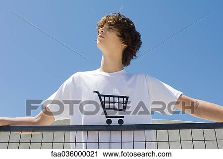 Teenage boy wearing tee-shirt printed with shopping cart, standing at railing, looking up View Large Photo Image Stock Image - Teenage boy wearing tee-shirt printed with shopping cart, standing at railing, looking up. Fotosearch