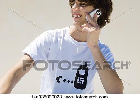 Teenage boy wearing tee-shirt printed with cell phone graphic, using cell phone, smiling View Large Photo Image Stock Image - Teenage boy wearing tee-shirt printed with cell phone graphic, using cell phone, smiling. Fotosearch