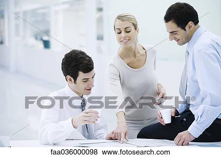Three professionals taking a coffee break, woman pointing at newspaper View Large Photo Image Stock Photo - Three professionals taking a coffee break, woman pointing at newspaper. Fotosearch