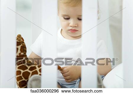 Stock Photograph - Toddler sitting in crib, playing with stuffed giraffe. Fotosearch