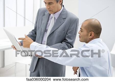 Two businessmen looking at laptop computer together in office View Large Photo Image Picture - Two businessmen looking at laptop computer together in office. Fotosearch