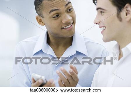 Two young businessmen chatting, one holding cell phone View Large Photo Image Stock Photography - Two young businessmen chatting, one holding cell phone. Fotosearch
