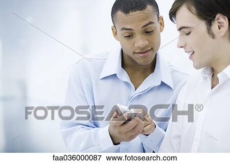 Two young businessmen looking down at cell phone View Large Photo Image Stock Photo - Two young businessmen looking down at cell phone. Fotosearch