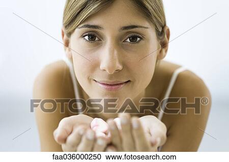 Stock Image - Woman holding handful of candy, smiling at camera, close-up. Fotosearch