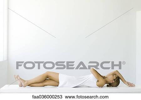 Stock Image - Woman lying on back, legs crossed, arms raised. Fotosearch