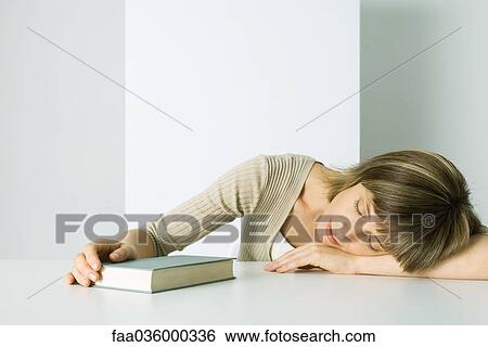 Stock Photograph - Woman resting head on arms, holding book, eyes closed. Fotosearch