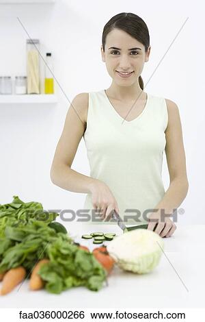 Woman slicing cucumber, assorted vegetables in foreground, smiling at camera View Large Photo Image Stock Photograph - Woman slicing cucumber, assorted vegetables in foreground, smiling at camera. Fotosearch