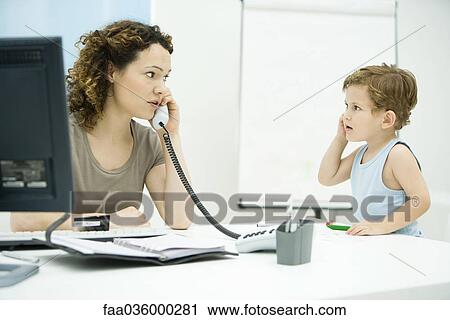 Stock Image - Woman using phone, young son imitating her, looking at each other. Fotosearch