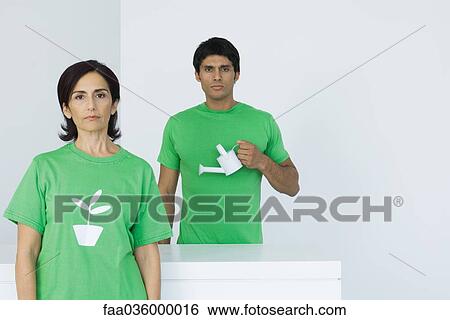 Woman wearing tee-shirt with plant graphic, man holding watering can in background View Large Photo Image Stock Photograph - Woman wearing tee-shirt with plant graphic, man holding watering can in background. Fotosearch