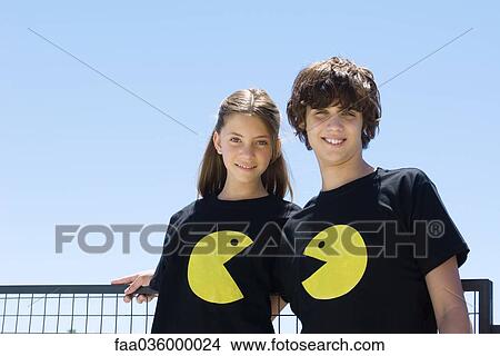 Young couple wearing tee-shirts printed with graphic characters, smiling at camera View Large Photo Image Picture - Young couple wearing tee-shirts printed with graphic characters, smiling at camera. Fotosearch