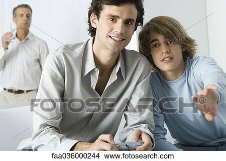 Young man and teen brother playing video game, looking at camera View Large Photo Image Picture - Young man and teen brother playing video game, looking at camera. Fotosearch
