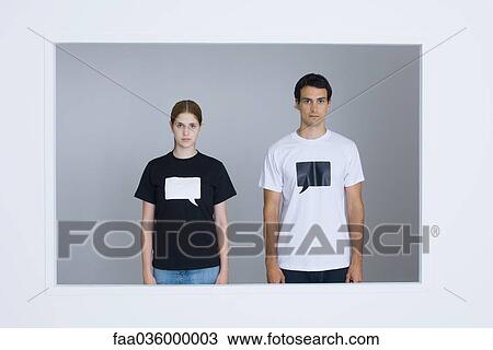Stock Image - Young man and young woman wearing tee-shirts printed with blank word bubbles, looking at camera. Fotosearch
