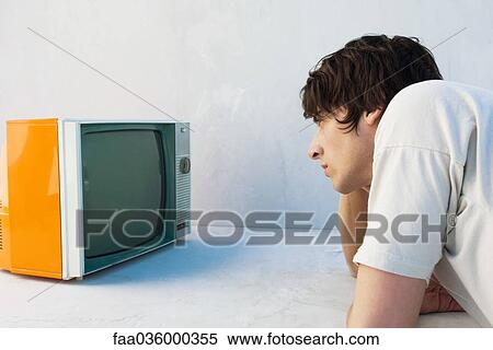 Young man leaning on elbow, watching television View Large Photo Image Stock Photography - Young man leaning on elbow, watching television. Fotosearch