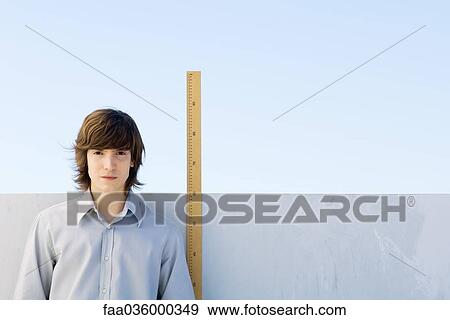 Young man measuring his height with ruler View Large Photo Image Stock Photo - Young man measuring his height with ruler. Fotosearch