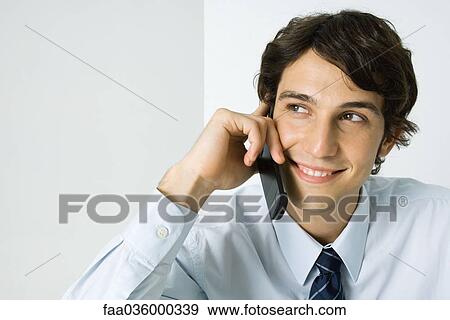 Young man using cell phone, looking away, smiling View Large Photo Image Stock Photo - Young man using cell phone, looking away, smiling. Fotosearch
