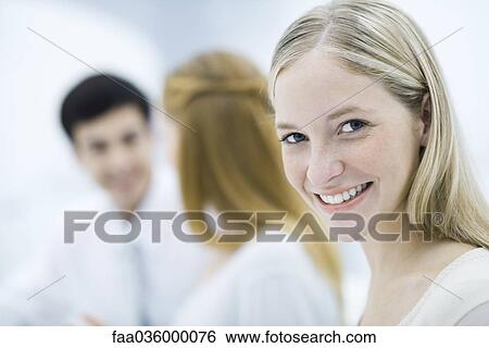 Young professional woman smiling at camera, colleagues talking in background View Large Photo Image Stock Photograph - Young professional woman smiling at camera, colleagues talking in background. Fotosearch