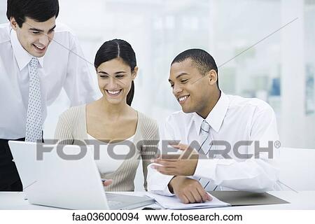 Young professionals looking at laptop computer together, smiling View Large Photo Image Picture - Young professionals looking at laptop computer together, smiling. Fotosearch
