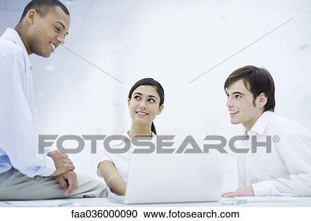 Young professionals sitting around laptop computer, smiling View Large Photo Image Stock Image - Young professionals sitting around laptop computer, smiling. Fotosearch