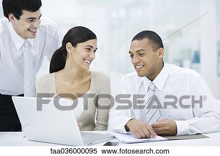 Young professionals sitting around laptop computer, smiling View Large Photo Image Stock Photography - Young professionals sitting around laptop computer, smiling. Fotosearch