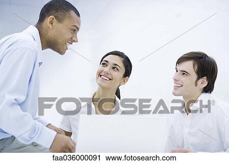 Young professionals smiling at each other, sitting near laptop View Large Photo Image Stock Image - Young professionals smiling at each other, sitting near laptop. Fotosearch