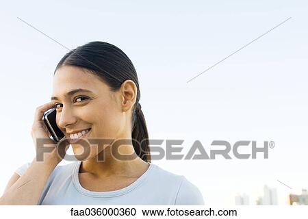 Young woman talking on cell phone, smiling at camera View Large Photo Image Stock Image - Young woman talking on cell phone, smiling at camera. Fotosearch