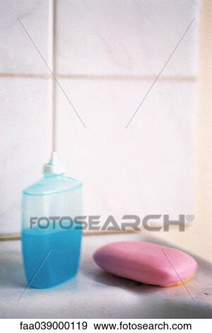Stock Photo - Bottle of blue liquid soap, pink bar of soap set on bathroom ledge. Fotosearch