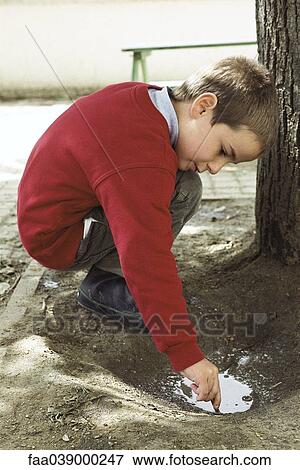 Boy crouching, playing in puddle, side view View Large Photo Image Stock Photo - Boy crouching, playing in puddle, side view. Fotosearch