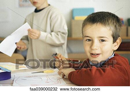 Stock Image - Boy drawing at desk, smiling at camera. Fotosearch