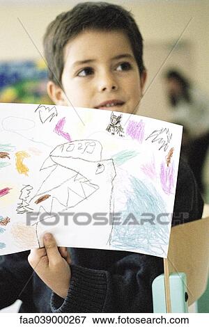 Stock Photo - Boy holding up drawing in class room. Fotosearch