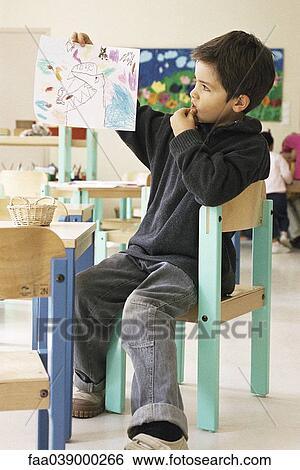 Stock Photograph - Boy holding up drawing in class room. Fotosearch
