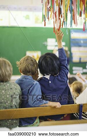 Stock Image - Child raising hand in class, rear view. Fotosearch
