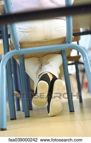 Stock Image - Child sitting in chair, legs crossed at ankle, low angle view. Fotosearch