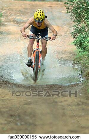 Stock Photography - Cyclist riding through puddle on mountain bike. Fotosearch