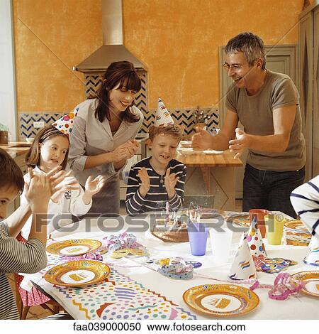 Stock Image - Family clapping around birthday cake after blowing out candles. Fotosearch