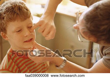 Stock Photo - Father putting ointment on boy's face. Fotosearch