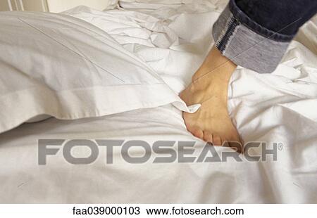 Stock Image - Foot of person standing on unmade bed, cropped view. Fotosearch