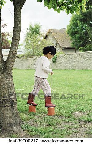 Stock Photo - Little girl using plastic buckets as stilts, side view. Fotosearch
