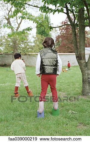 Stock Photo - Little girls using plastic buckets as stilts, rear view. Fotosearch