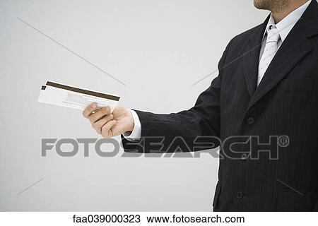 Stock Image - Man in suit holding out tickets, side view. Fotosearch