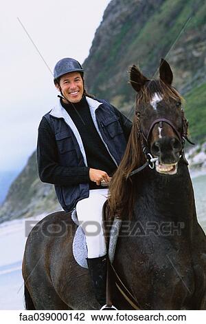 Stock Image - Man riding horse on beach, portrait. Fotosearch